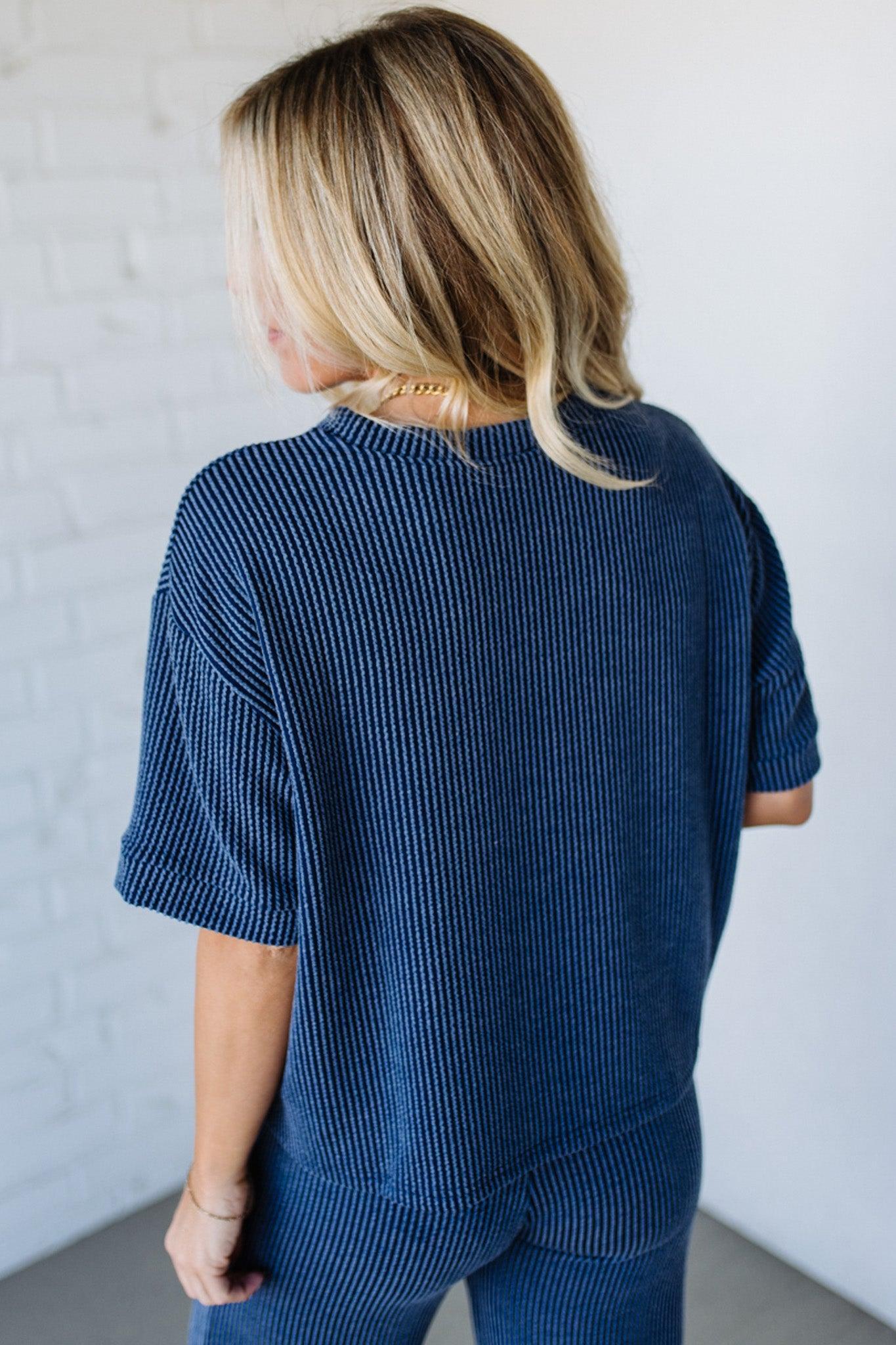 Person wearing a blue ribbed sweater and pants against a white wall