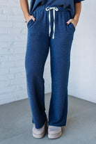 Person wearing blue checkered pants with a white drawstring against a white brick wall.