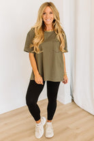 Woman wearing an olive green t-shirt, black leggings, and white sneakers in a minimalistic setting.