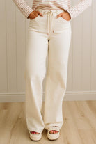 Person wearing white wide-leg pants and a striped shirt against a neutral background