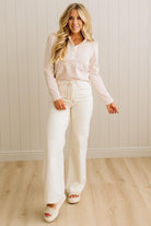 Woman wearing a striped shirt and white pants standing against a light wooden paneled wall.