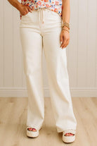 Person wearing white wide-leg pants and a floral top against a light wooden panel background