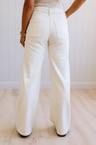 Person wearing white pants on a light wooden floor with a white wall background