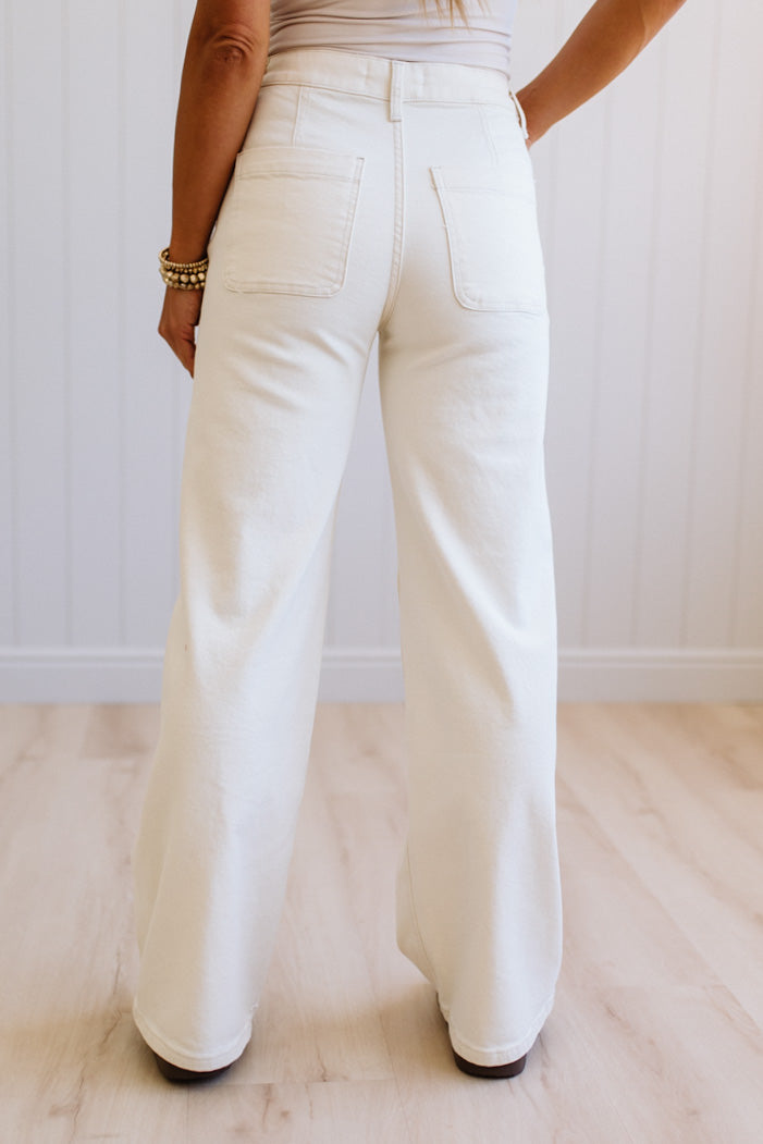 Person wearing white pants on a light wooden floor with a white wall background
