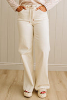 Person wearing white wide-leg pants and a striped shirt against a neutral background