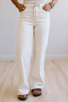 Person wearing white flared jeans and sandals on a light wooden floor.