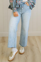 Person wearing floral blouse, light blue jeans, and white shoes on a wooden floor.