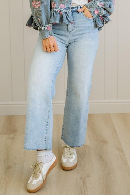 Person wearing floral blouse, light blue jeans, and white shoes on a wooden floor.