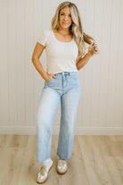 Woman wearing a white t-shirt and light blue jeans standing against a plain background