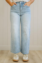 Person wearing light blue jeans and white sneakers against a neutral background