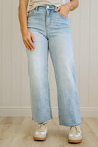 Person wearing light blue jeans and white sneakers in a neutral setting