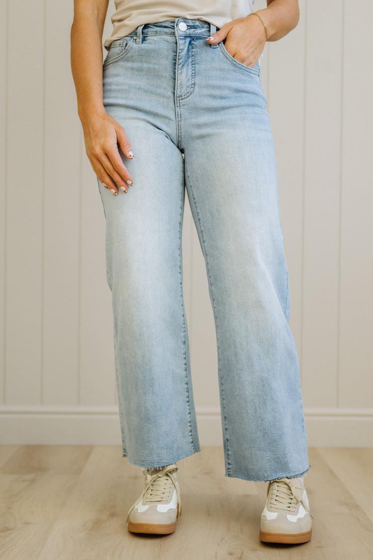 Person wearing light blue jeans and white sneakers in a neutral setting