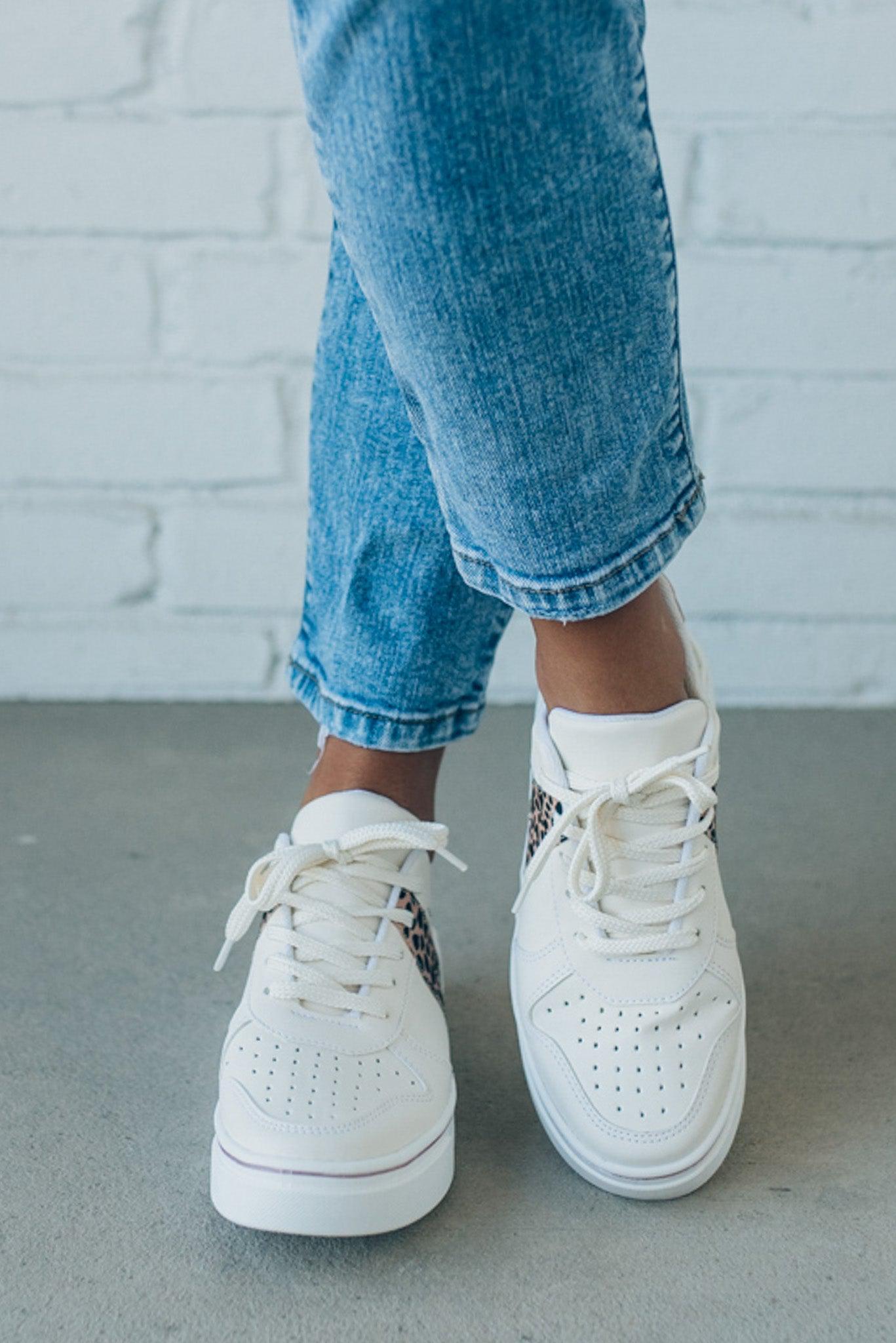 woman wearing creamy white sneakers with a leopard accent on the side.