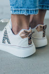 woman wearing creamy white sneakers with a leopard accent on the side.