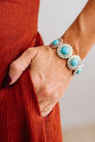 Close up of womans arm with her hand in a pocket of a rust red dress, showing a Western Concho Turquoise Stretch Bracelet