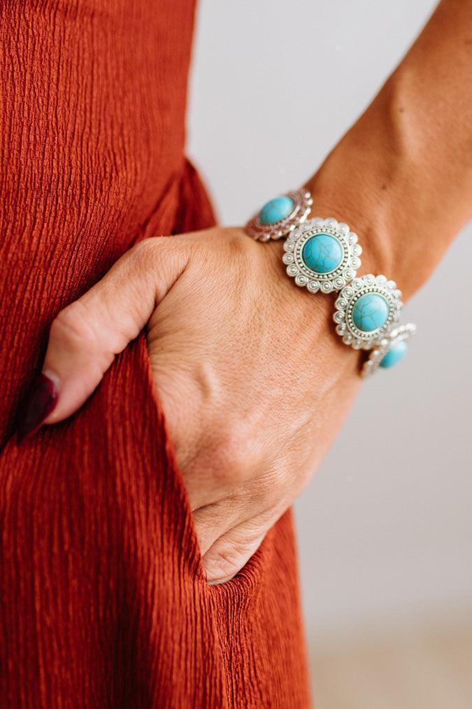 Close up of womans arm with her hand in a pocket of a rust red dress, showing a Western Concho Turquoise Stretch Bracelet