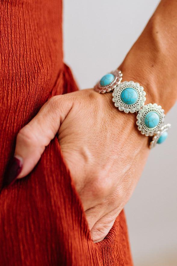 Close up of womans arm with her hand in a pocket of a rust red dress, showing a Western Concho Turquoise Stretch Bracelet