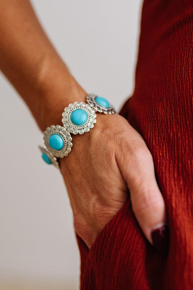 Close up of womans arm with her hand in a pocket of a rust red dress, showing a Western Concho Turquoise Stretch Bracelet