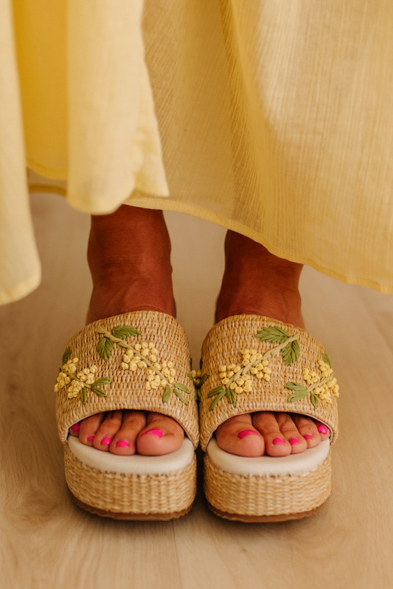 Woman wearing woven raffia base platforms that are detailed with floral embroidery.