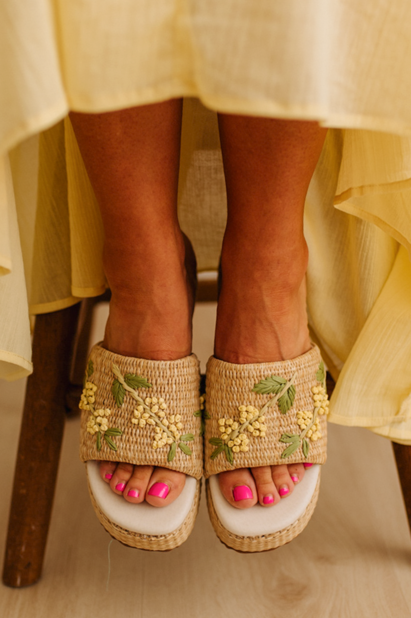 Woman wearing woven raffia base platforms that are detailed with floral embroidery.