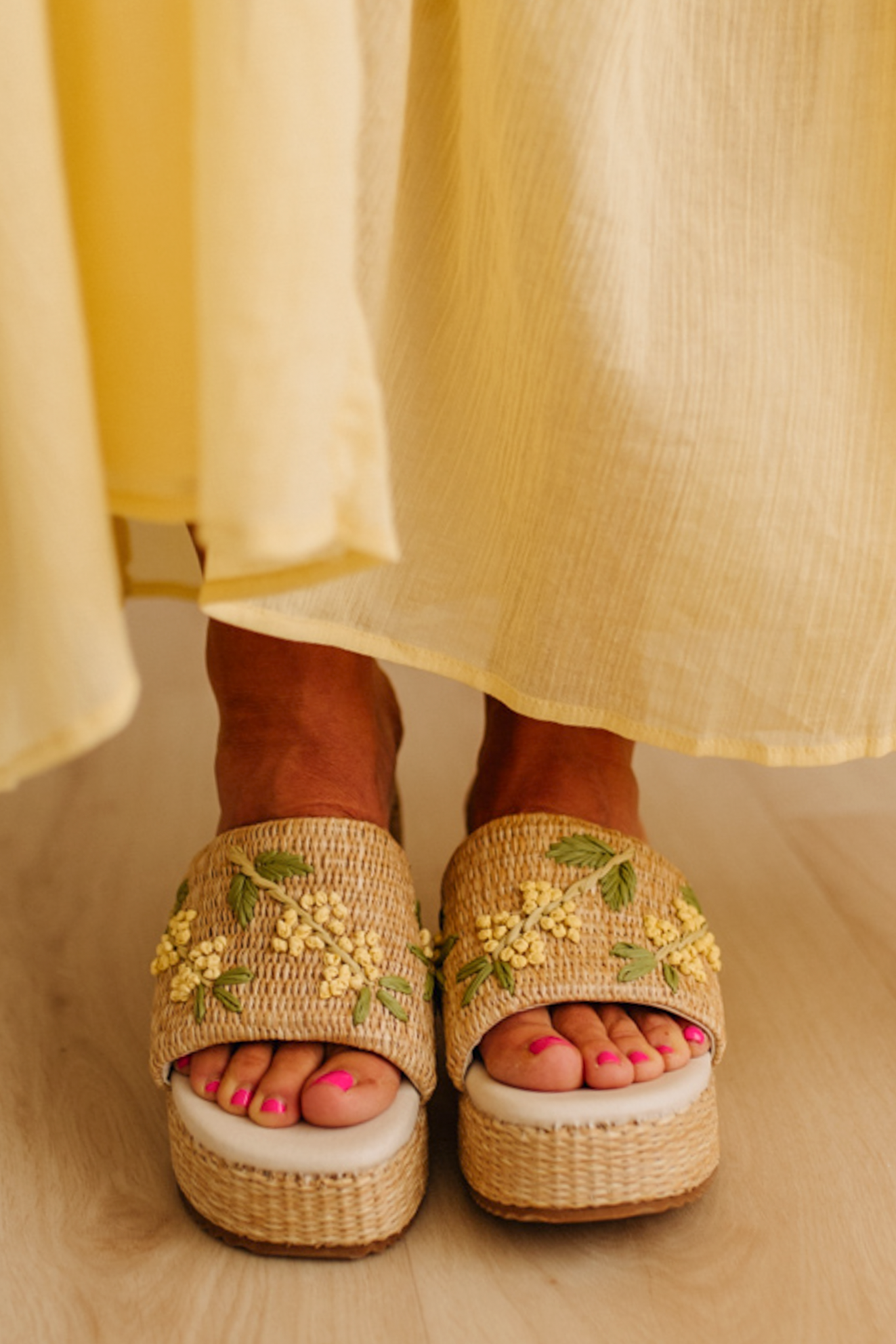 Woman wearing woven raffia base platforms that are detailed with floral embroidery.