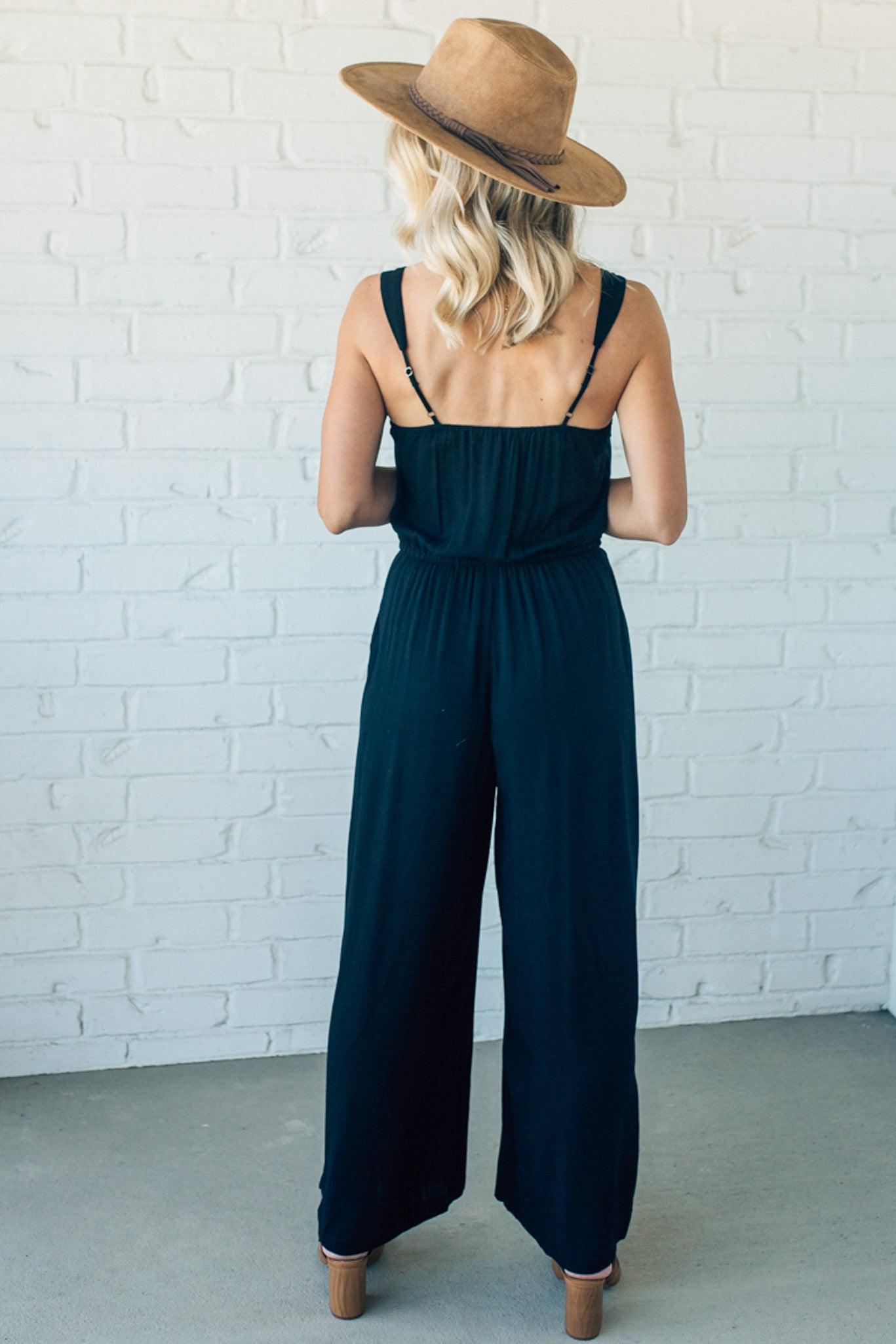 Women wearing a black wide leg jumpsuit with tie waist and pockets.