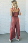 Women wearing a rust colored wide leg jumpsuit with tie waist and pockets.