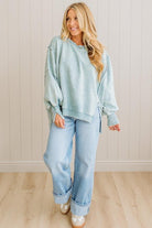 Woman wearing a light blue sweatshirt and jeans standing against a white paneled wall.