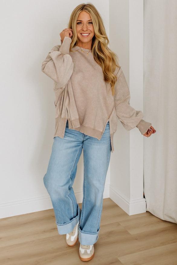 Woman wearing a beige sweater and blue jeans standing indoors.