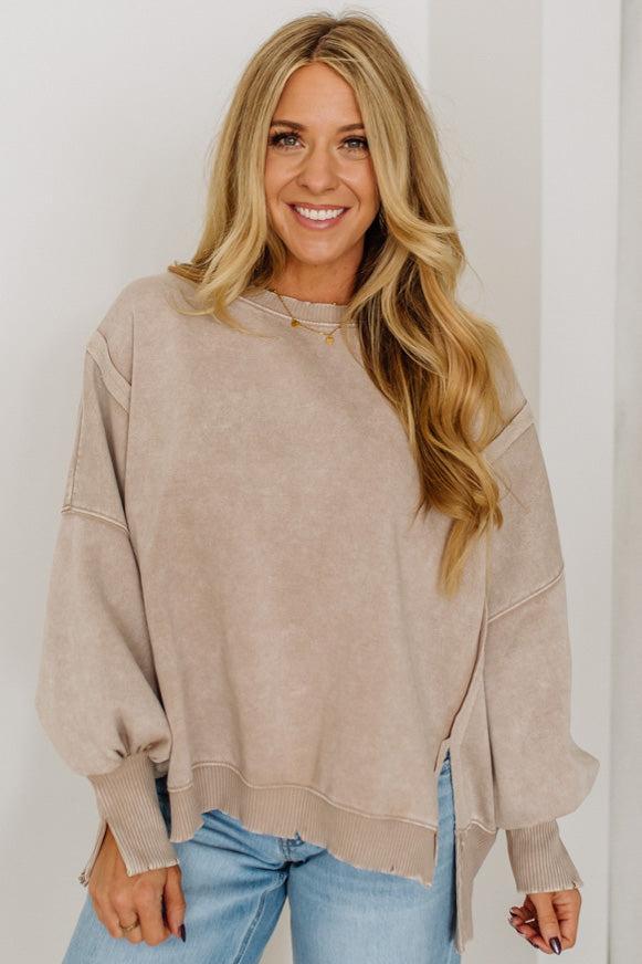 Woman wearing a beige sweater and light blue jeans against a plain background