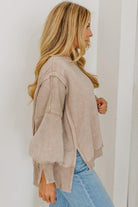 Woman wearing a beige jacket and blue jeans against a white wall