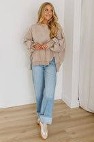 Woman wearing a beige sweater and light blue jeans indoors.