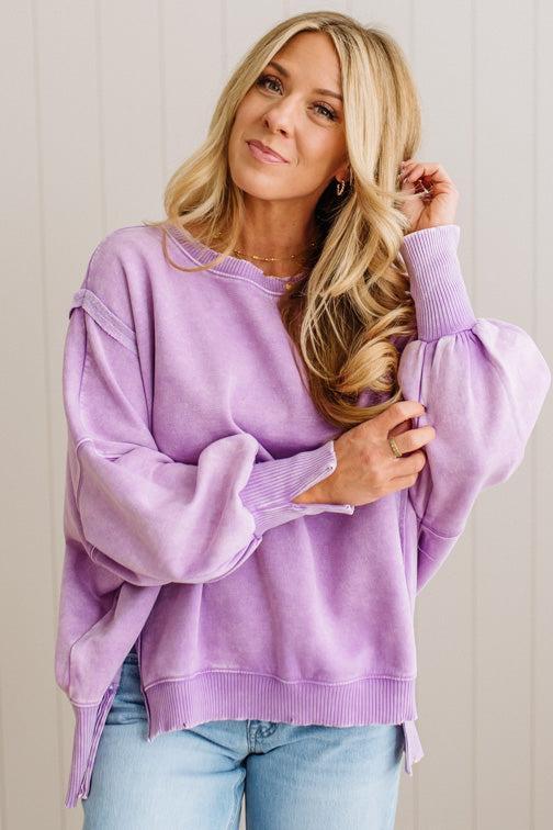 Woman wearing a purple sweater and light blue jeans against a plain background