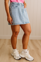 Person wearing a light blue denim skirt and white sneakers on a wooden floor.