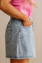 Person wearing a pink top and denim skirt on a neutral background
