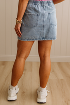 Person wearing a denim skirt and white sneakers on a wooden floor.