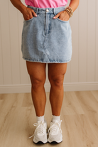 Person wearing a light blue denim skirt, white sneakers, and a pink top on a wooden floor.