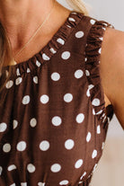 Close-up of a brown sleeveless top with white polka dots and ruffled trim, worn by a model.