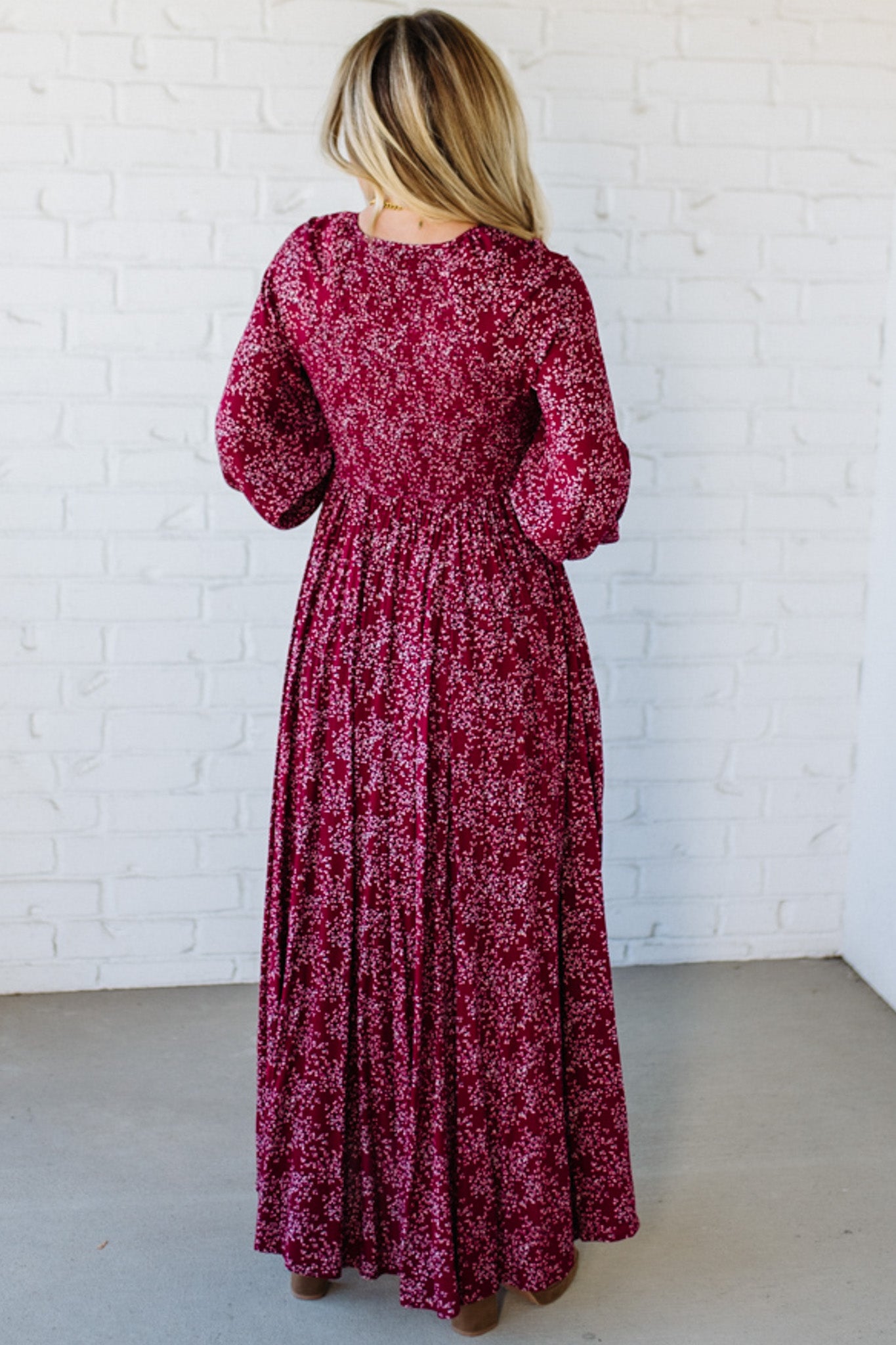 Blonde Woman Wearing a Smocked Floral Maxi Dress with Button Front and v-neckline in a deep wine red color.