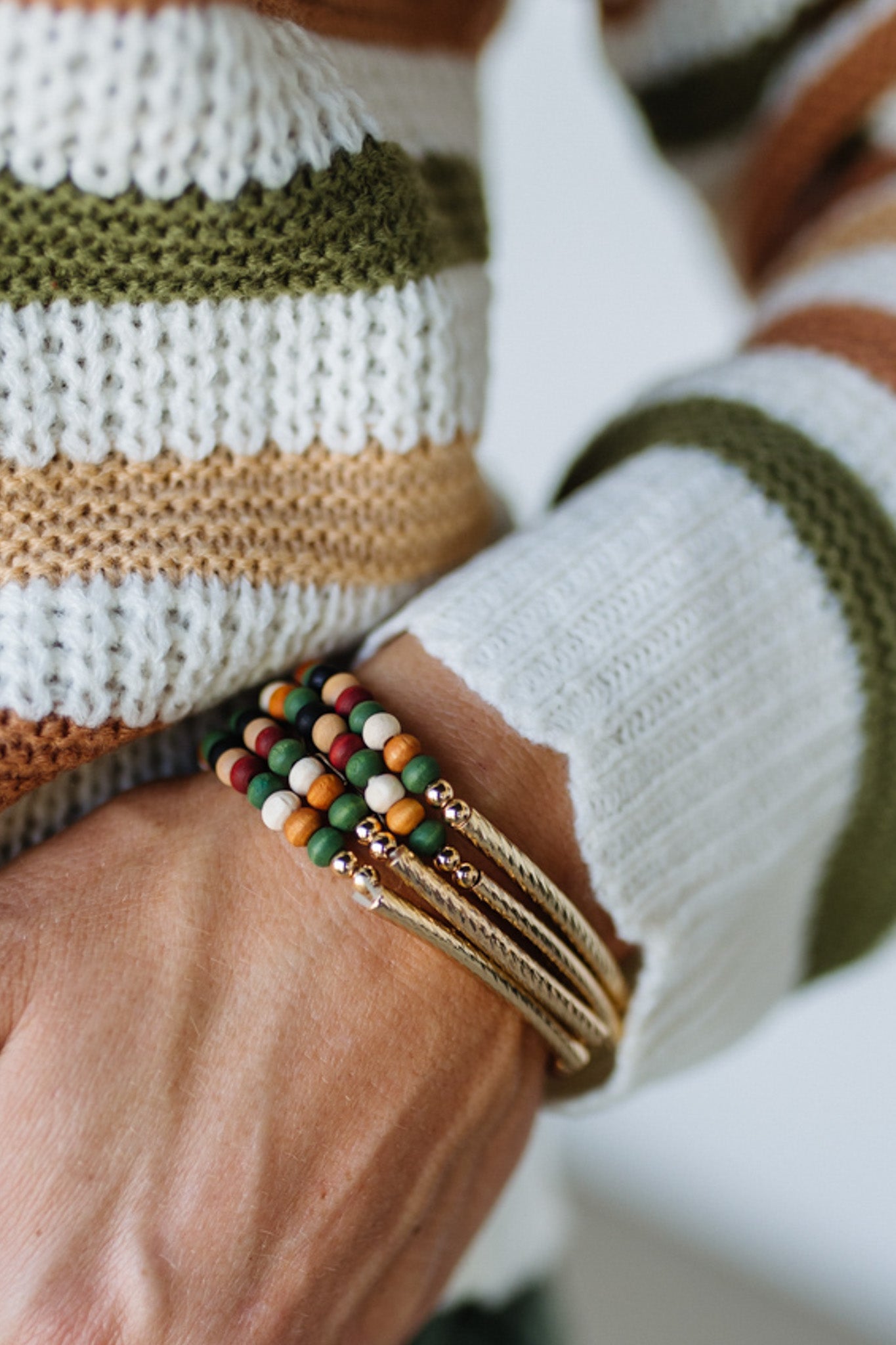 Close-up of a wrist wearing colorful beaded bracelets with a striped sweater background
