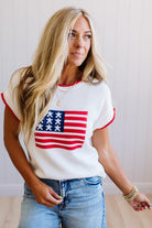 Woman wearing a white t-shirt with an American flag design and blue jeans.