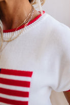 Close-up of a person wearing a white sweater with red and blue stripes.