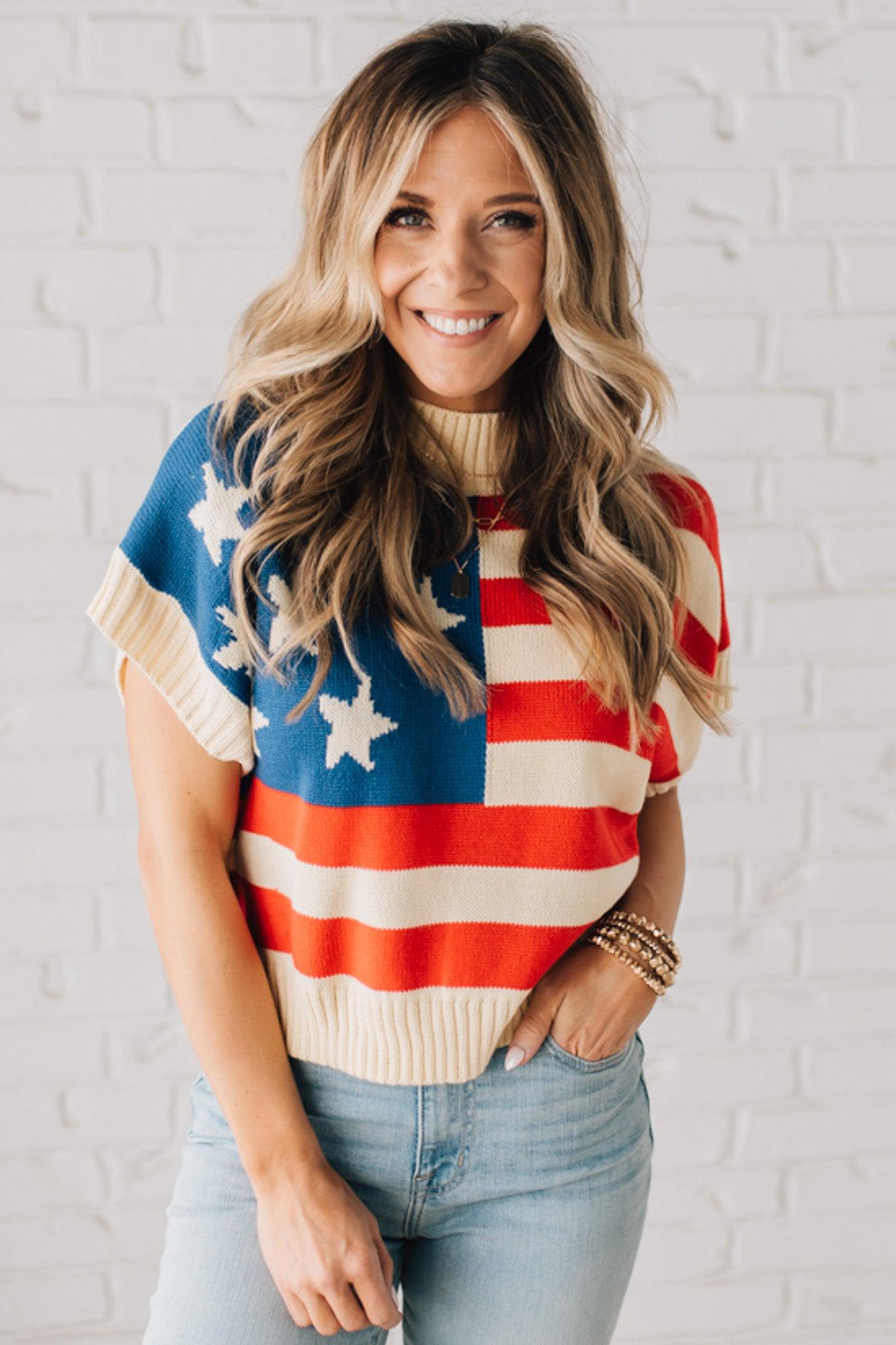 BLONDE WOMAN WEARING A WOVEN STAR AMERICAN FLAG THEME RIB BANDED SHORT SLEEVE SWEATER WITH MOCK NECKLINE.