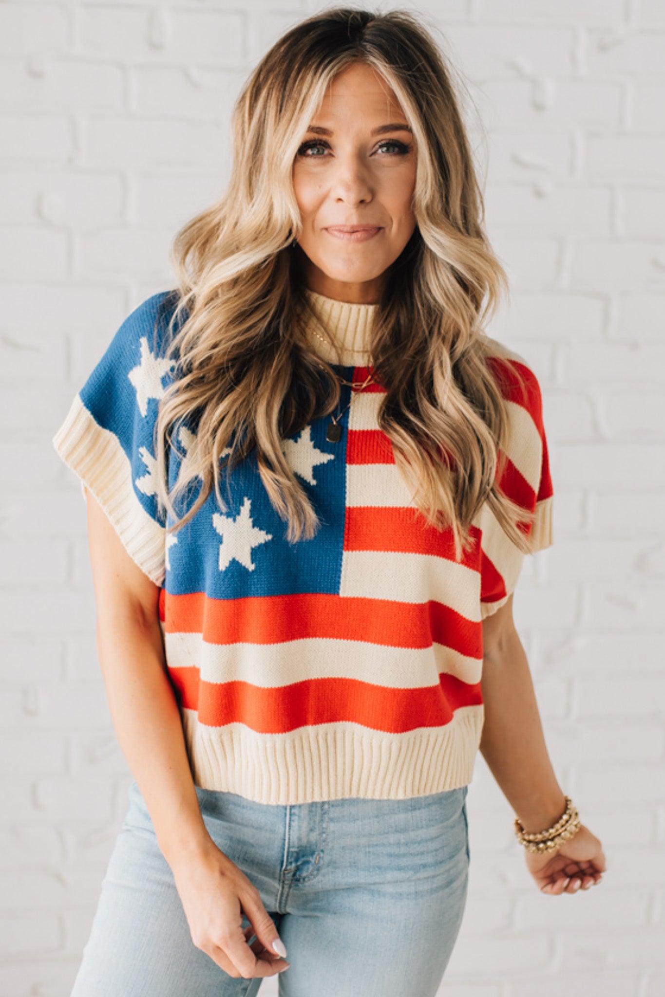 BLONDE WOMAN WEARING A WOVEN STAR AMERICAN FLAG THEME RIB BANDED SHORT SLEEVE SWEATER WITH MOCK NECKLINE.