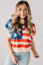 BLONDE WOMAN WEARING A WOVEN STAR AMERICAN FLAG THEME RIB BANDED SHORT SLEEVE SWEATER WITH MOCK NECKLINE.