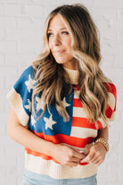 BLONDE WOMAN WEARING A WOVEN STAR AMERICAN FLAG THEME RIB BANDED SHORT SLEEVE SWEATER WITH MOCK NECKLINE.