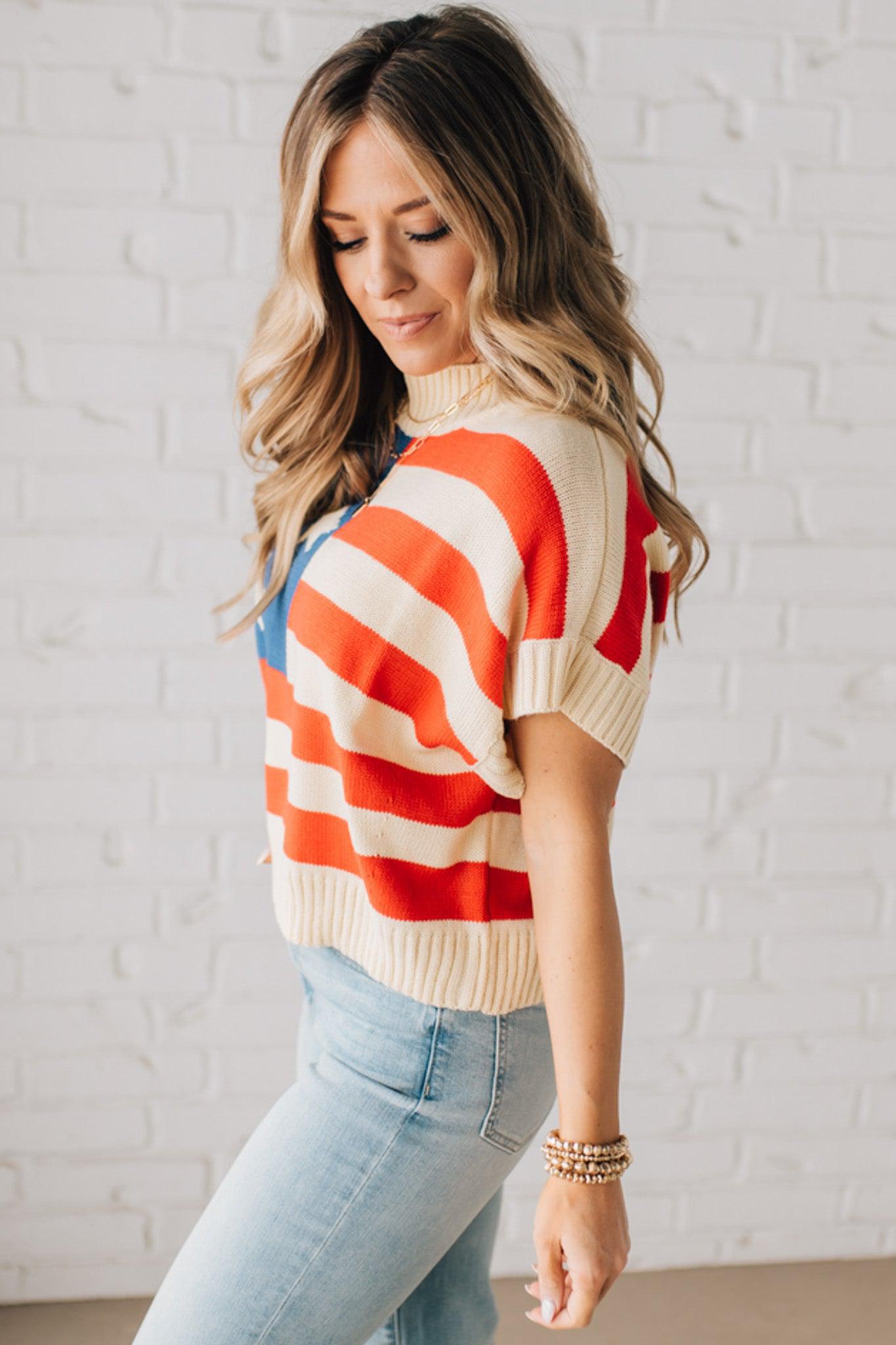 BLONDE WOMAN WEARING A WOVEN STAR AMERICAN FLAG THEME RIB BANDED SHORT SLEEVE SWEATER WITH MOCK NECKLINE.