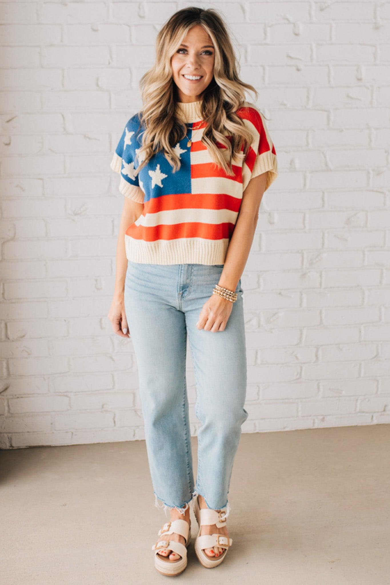 BLONDE WOMAN WEARING A WOVEN STAR AMERICAN FLAG THEME RIB BANDED SHORT SLEEVE SWEATER WITH MOCK NECKLINE.