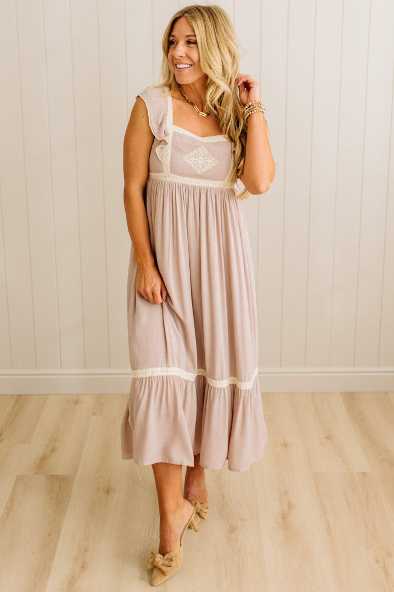 Woman wearing a light pink dress with lace details against a white paneled wall.