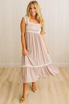 Woman wearing a light pink dress with white lace details in a room with wooden flooring and a white wall.